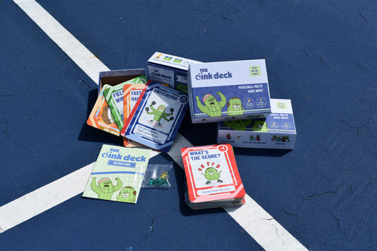 The Dink Deck pickleball card game box with the deck and action cards spread out on a pickleball court