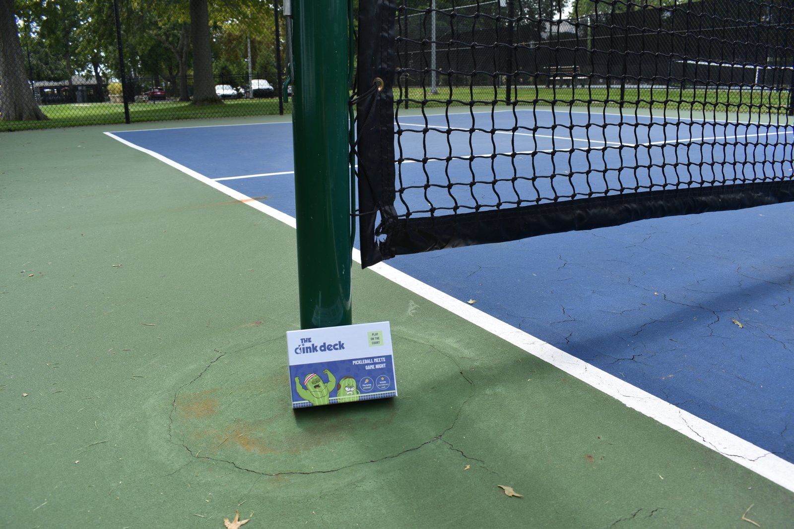 The Dink Deck box leaning on a pickleball net post