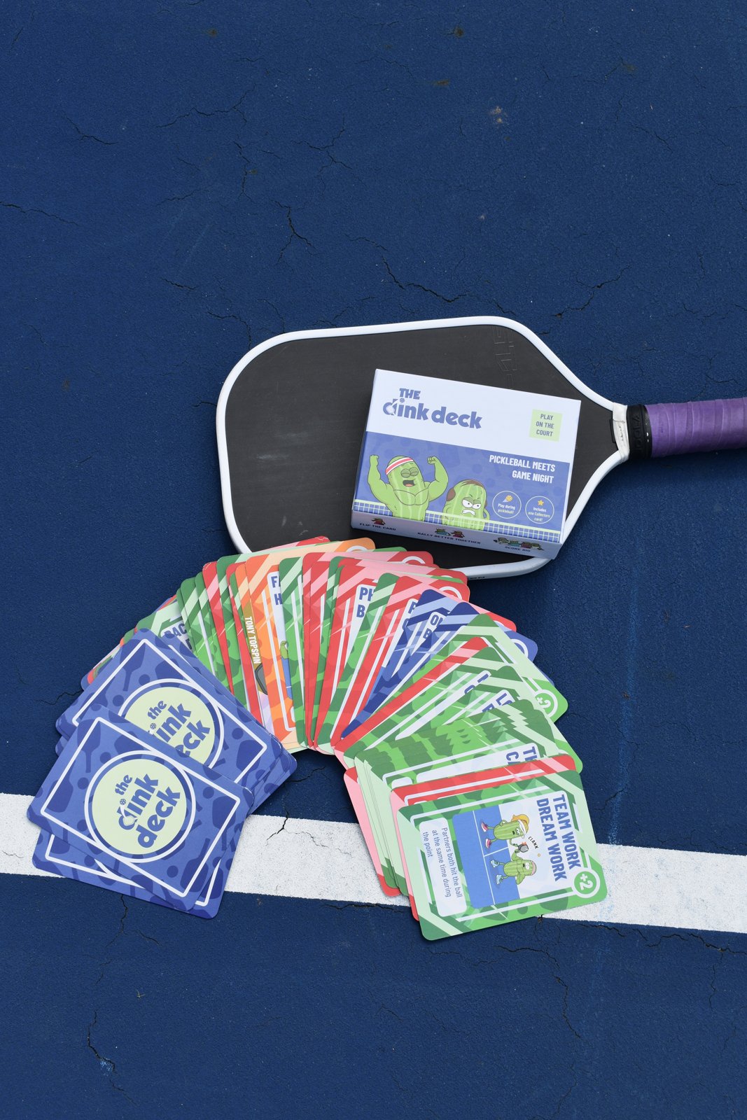 Paddle with The Dink Deck box and fanned-out cards on the court